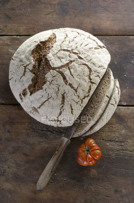 Una hogaza de pan fresco de campo, rebanado en una superficie de madera - foto de stock