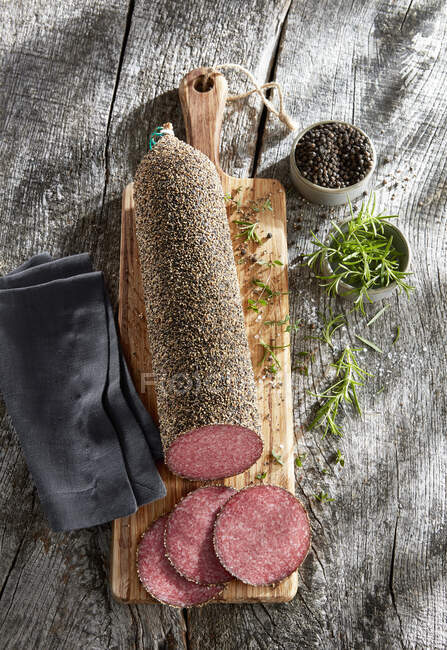 Whole pepper salami, sliced on a wooden board — Stock Photo