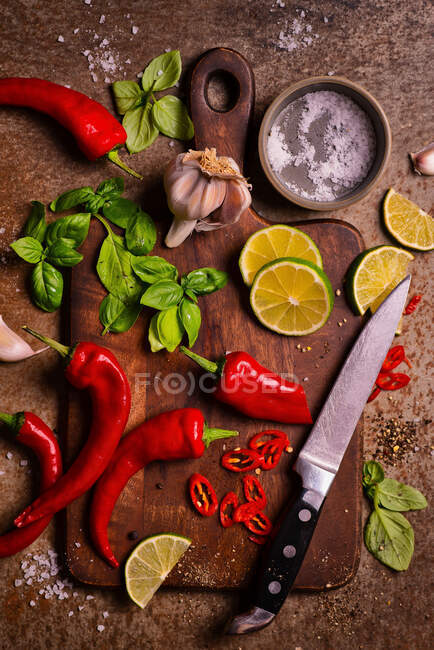 Chopping board with knife and chilli, basil, lime, garlic and salt — Stock Photo