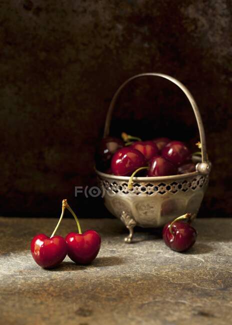 Fresh cherries in vintage metal bowl and on rustic surface — Stock Photo