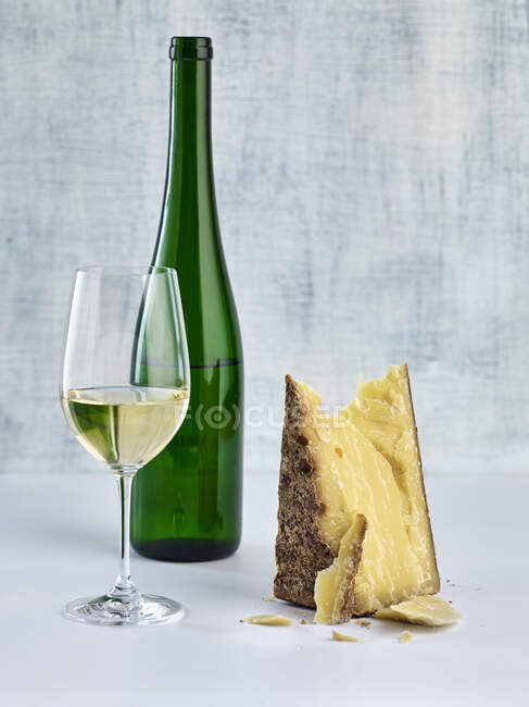Vidro e garrafa de vinho branco com pedaço de queijo duro — Fotografia de Stock