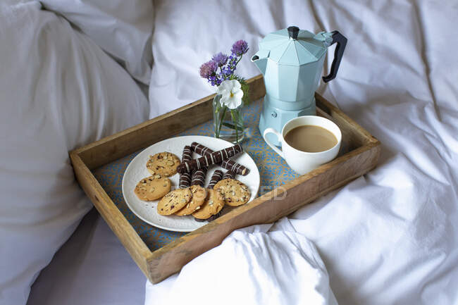 Un plateau de petit déjeuner avec biscuits et café au lit — Photo de stock
