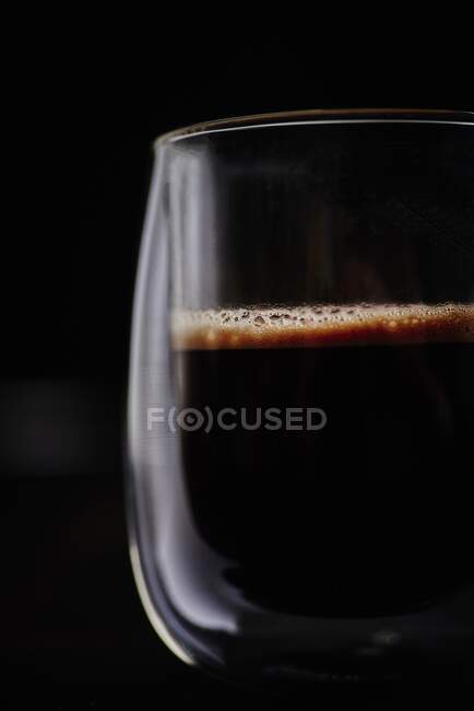 Uma xícara de café preto acabado de fazer na frente de um fundo preto — Fotografia de Stock