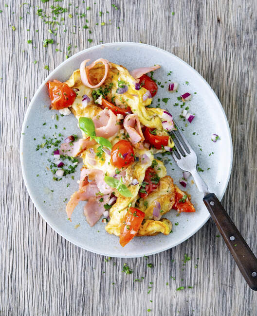 Omelet with ham, tomatoes and greens and fork on plate — Stock Photo