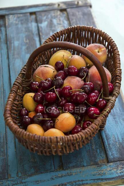 Fresh apricots, peaches and cherries in a basket — Stock Photo