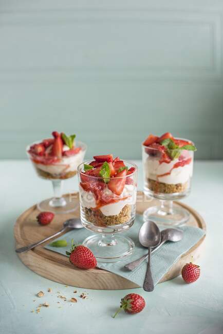 Strawberry and vanilla cheesecakes with a nutty biscuit base served in small glasses — Stock Photo