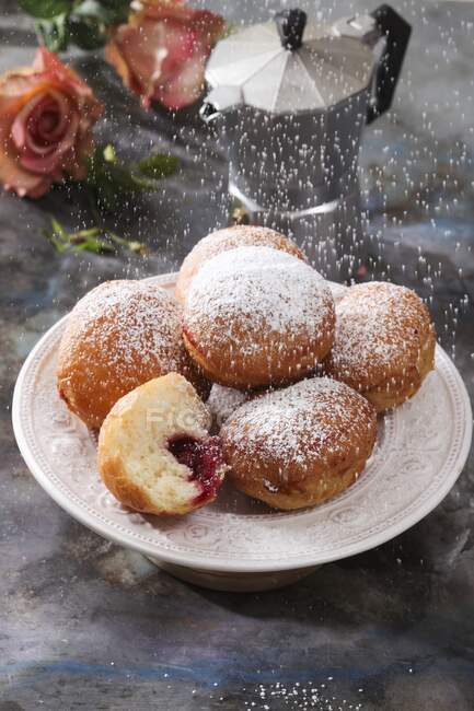 Icing sugar being sifted over a plate of jam doughnuts — Stock Photo