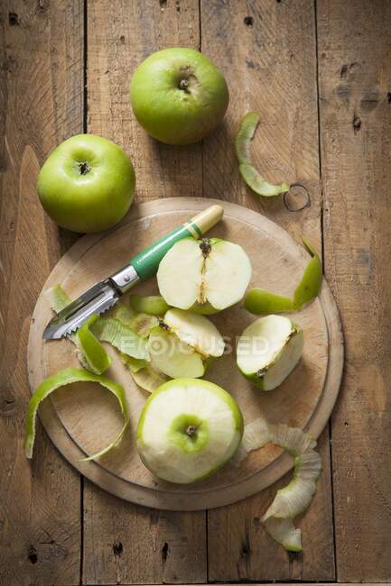 Manzanas Bramley verdes, enteras y peladas, con pelador de manzanas - foto de stock