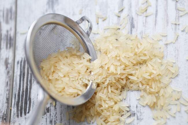 Long-grain rice in a sieve and on a wooden background — Stock Photo