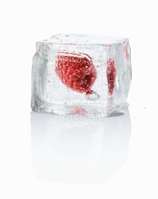 Ice cube with fresh raspberry on white background with reflection — Stock Photo