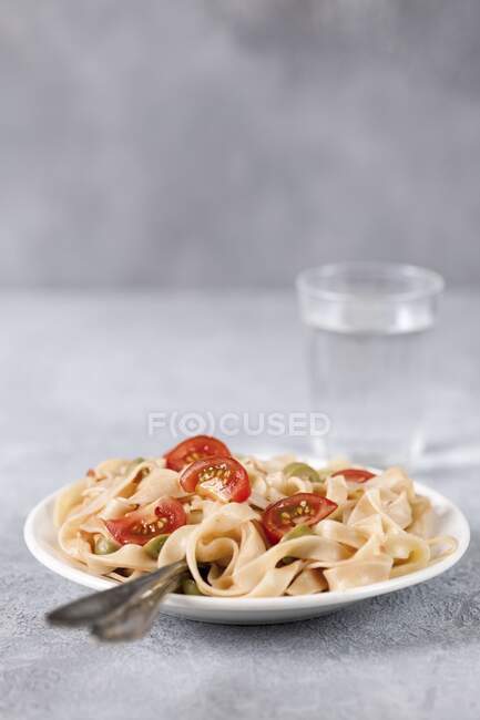Tagliatelle con tomates y aceitunas, cubiertos en plato - foto de stock