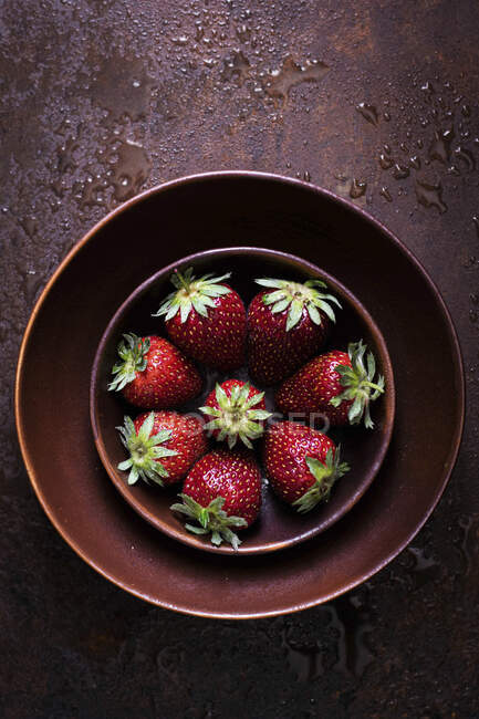 Fresh strawberries in clay bowls on wet metal surface — Stock Photo