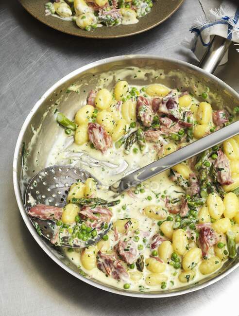 Gnocchi en sauce crème au jambon, asperges vertes et petits pois — Photo de stock