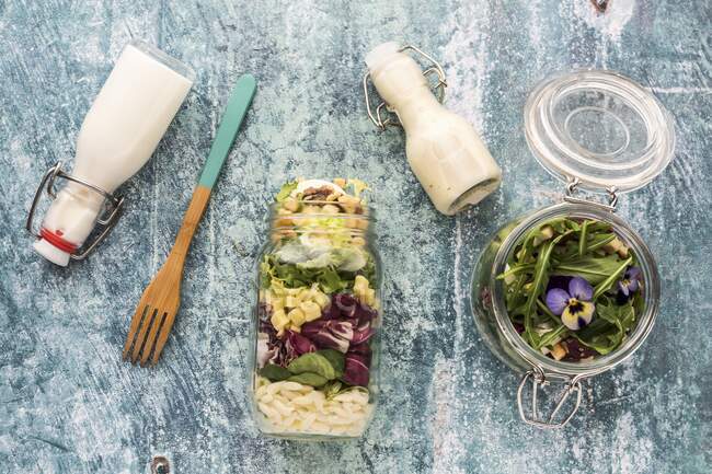 Quinoa and orzo pasta salads in glass jars, with dressing and a wooden fork — Photo de stock