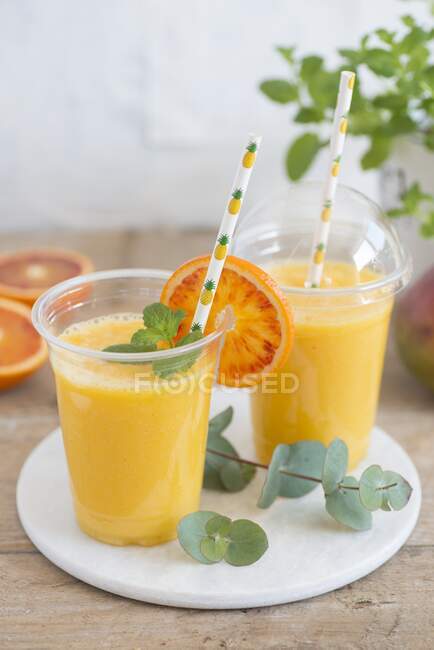 Piña, mango y zumo de naranja en tazas para llevar - foto de stock