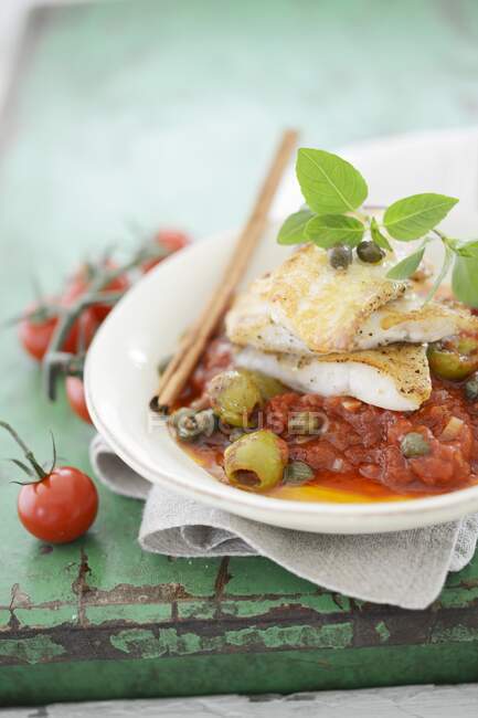 Fish fillets on tomatoes with green olives — Stock Photo