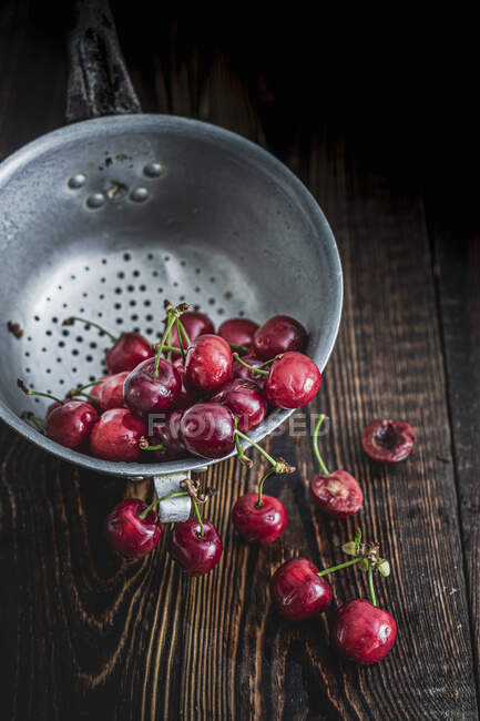 Cherries in metal colander and on wooden surface — Stock Photo