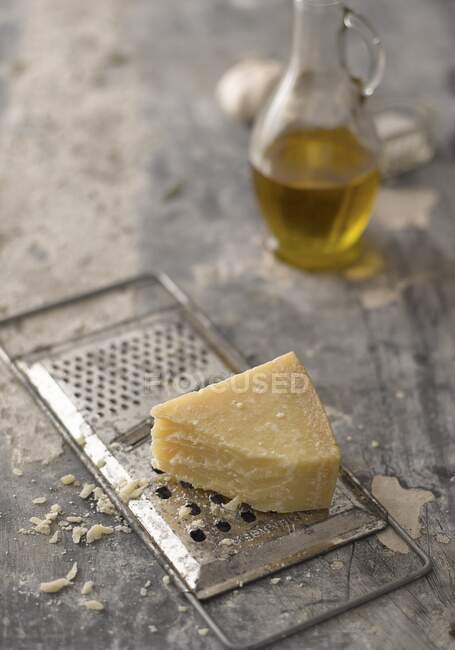Pezzo di parmigiano su grattugia di formaggio di metallo con brocca di olio su sfondo — Foto stock