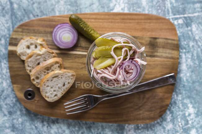 Eine Wurst, roter Zwiebel- und Gurkensalat im Glas auf einem Holzbrett mit Baguette-Scheiben — Stockfoto
