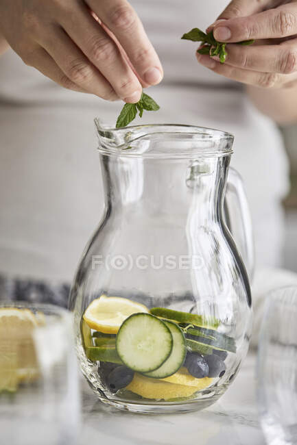 Ajouter des feuilles de menthe dans une cruche pour l'eau froide infusée — Photo de stock