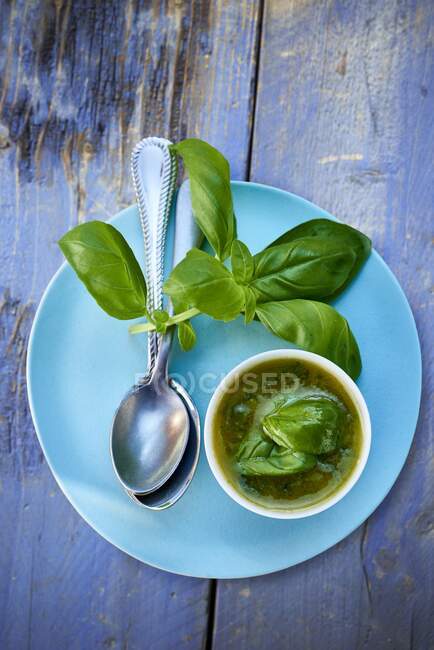 Vinaigrette di basilico in una piccola ciotola, foglie di basilico e un cucchiaio su un piatto blu — Foto stock