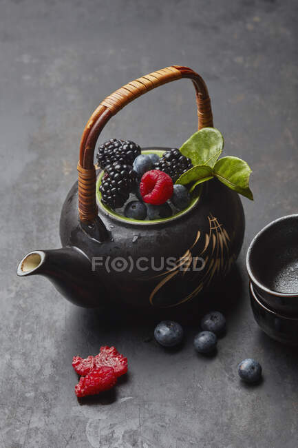 Чайник зі свіжими ягодами та чайним листям — стокове фото