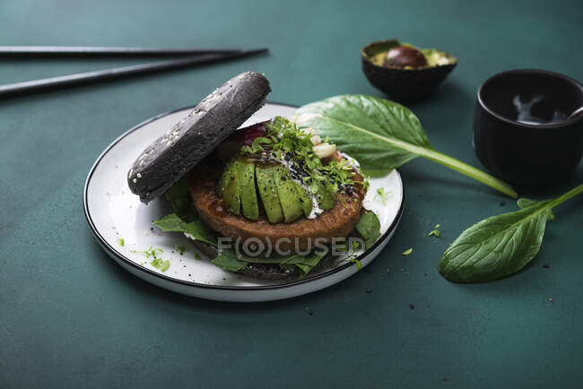Soy wheat protein patty with avocado, radishes and two sauces in a black burger bun — Stock Photo