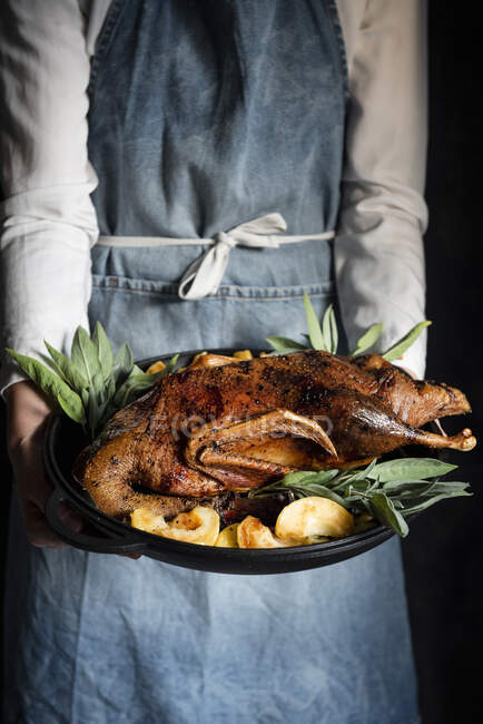 Frau serviert gebratene Ente mit Bratäpfeln und Salbei — Stockfoto