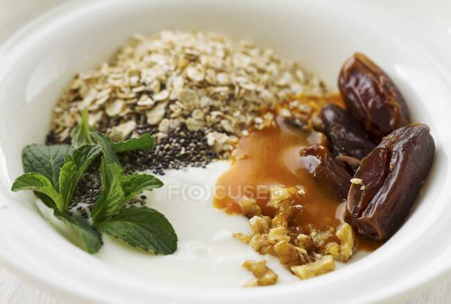 Yoghurt with dates, chia seeds, oatmeal, nuts, fruit sauce and mint — Stock Photo