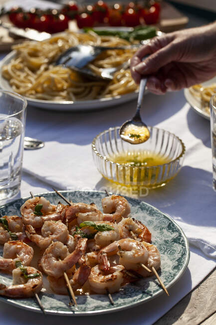 Garnelenspieße mit Basilikumbutter-Sauce, Pasta cacio e pepe, Pasta mit Käse und Pfeffer und Tomaten auf einem Tisch im Freien — Stockfoto