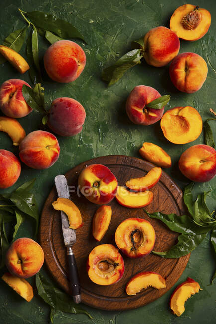 Frische Pfirsiche mit Blättern auf Holzbrett mit Messer und auf grüner Oberfläche — Stockfoto