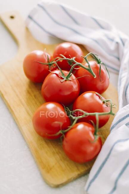 Tomates en rama sobre tabla de madera - foto de stock