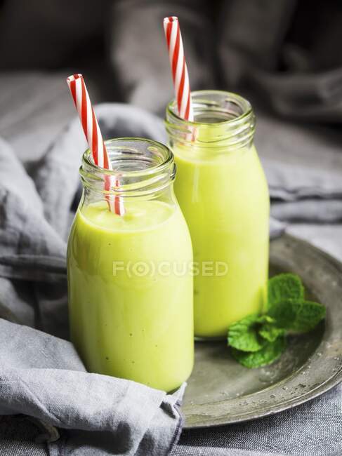Vegan green smoothies in glass bottles with straws — Stock Photo