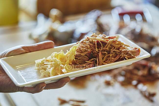 Carne di maiale tirata su un piatto di portata lungo in mano maschile — Foto stock