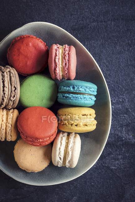 Biscuits au macaron sucrés et colorés dans l'assiette sur fond sombre — Photo de stock