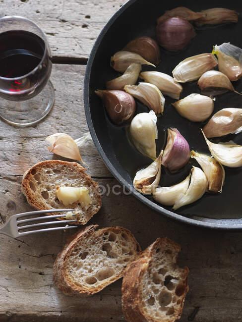 Pan-fried cloves of garlic with baguette bread — Stock Photo