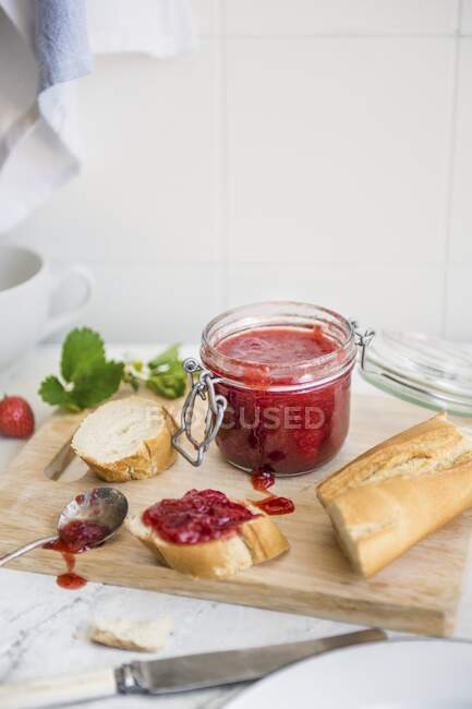 Strawberry jam in a glass jar, and spread on a slice of white bread — Stock Photo