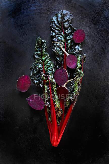 Red chard and beetroot halves in front of a black background — Stock Photo