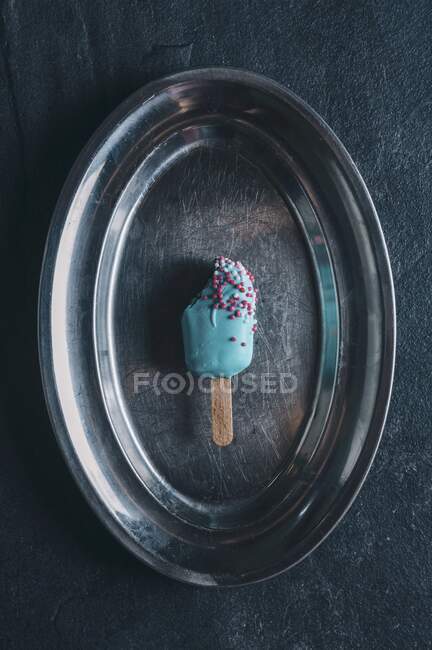 Un gâteau pop en forme de lolly glacé avec glaçage aux couleurs vives sur un plateau argenté — Photo de stock