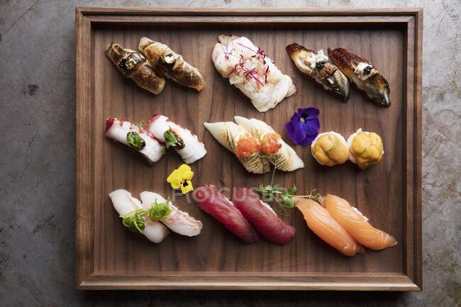 Plato de sushi de madera con varios filetes de pescado - foto de stock