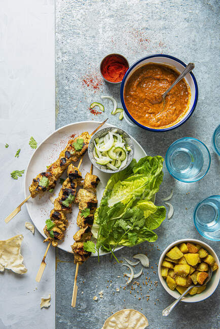 Chicken tikka skewers with masala sauce, bombay potatoes, pickled onion and cucumber salad and crunchy lettuce — Stock Photo
