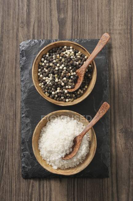 Poivre noir et blanc et gros sel de mer avec cuillères dans de petits bols — Photo de stock