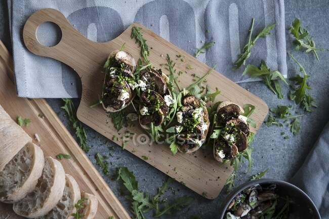 Bruschetta with mushrooms, feta and rocket on a wooden chopping board (seen from above) — Stock Photo