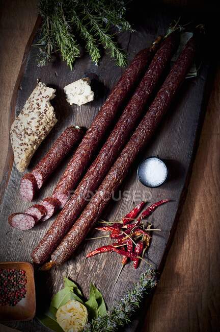 Embutidos largos de cerdo con rollos de linaza y chiles secos en una tabla de cortar de madera - foto de stock