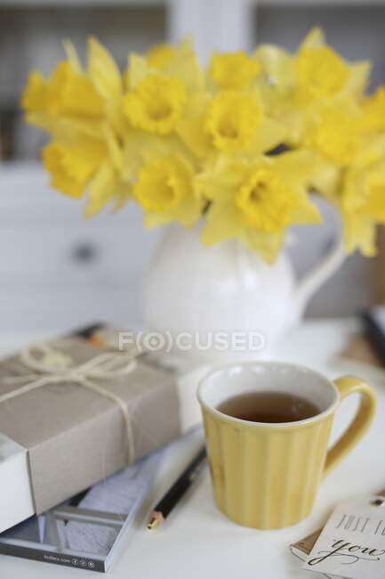 Close-up shot of delicious cup of tea and a vase of flowers — Stock Photo