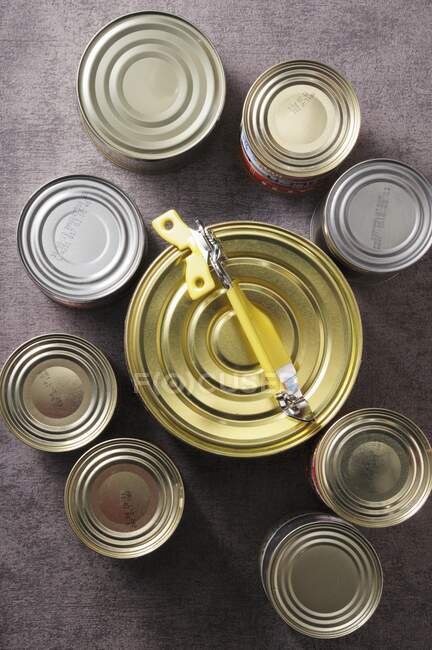 Varias latas de comida con un abrelatas (visto desde arriba) - foto de stock