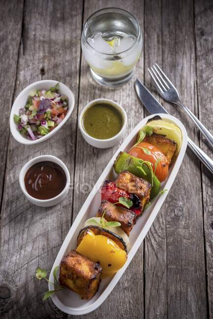 A paneer and vegetable skewer with different sauces — Stock Photo