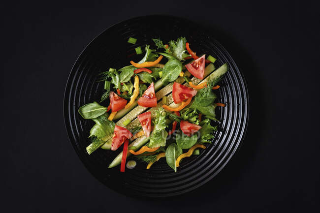 Salad with fresh vegetables and arugula on black background — Stock Photo
