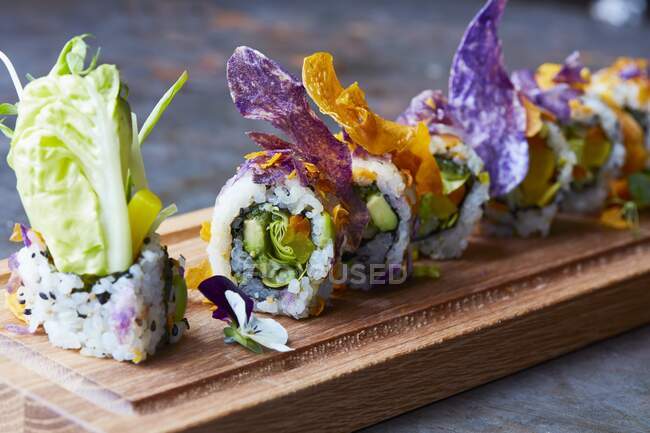 Sushi com legumes em um prato de madeira, decorado com flores comestíveis (Japão) — Fotografia de Stock