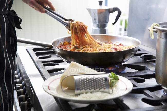 Uma pessoa que prepara linguine com molho de tomate em uma panela em um fogão — Fotografia de Stock
